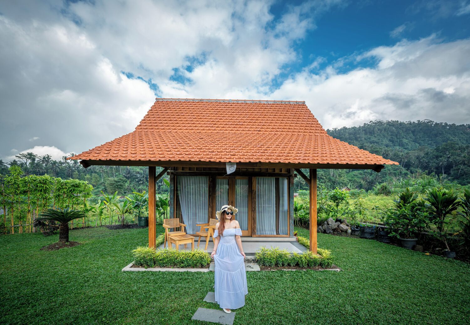 Un pavillon en bois, surmonté d’un toit de tuiles, entouré d’une végétation luxuriante et baigné par un ciel dégagé.