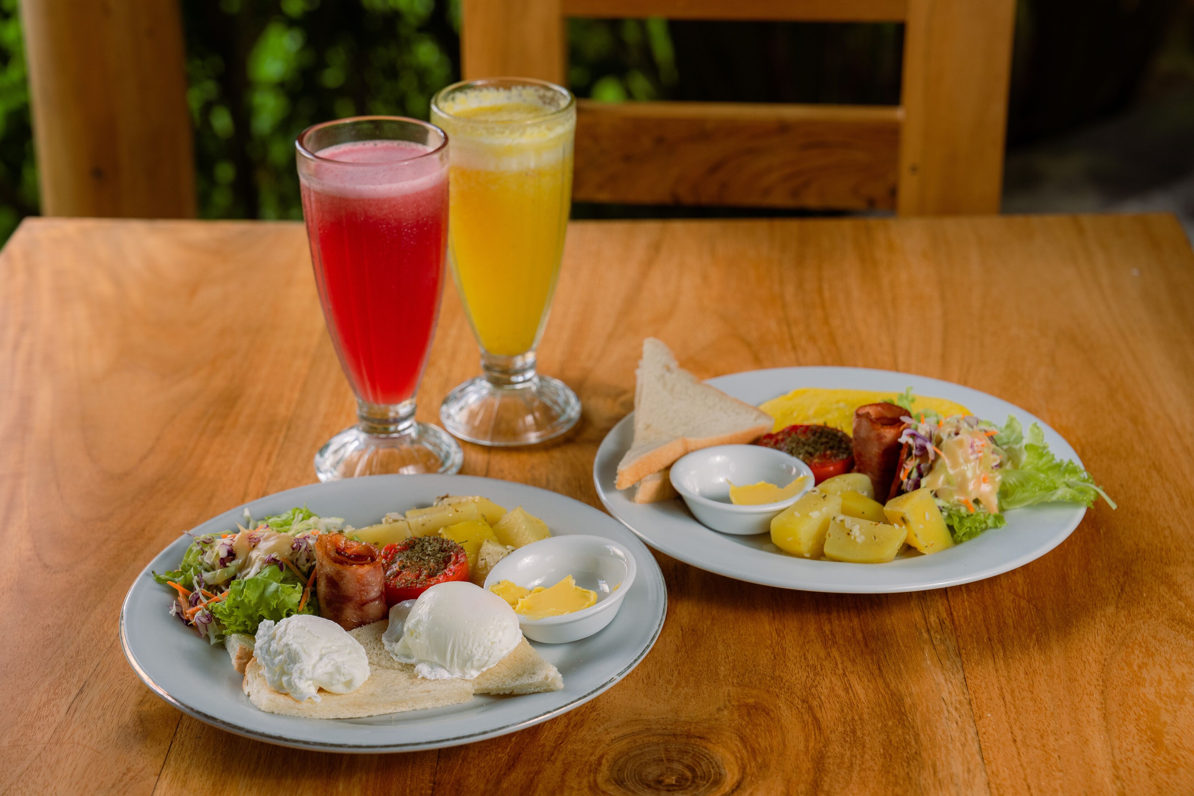 A wooden table with two plates of food, a glass of red juice, and a glass of orange juice.