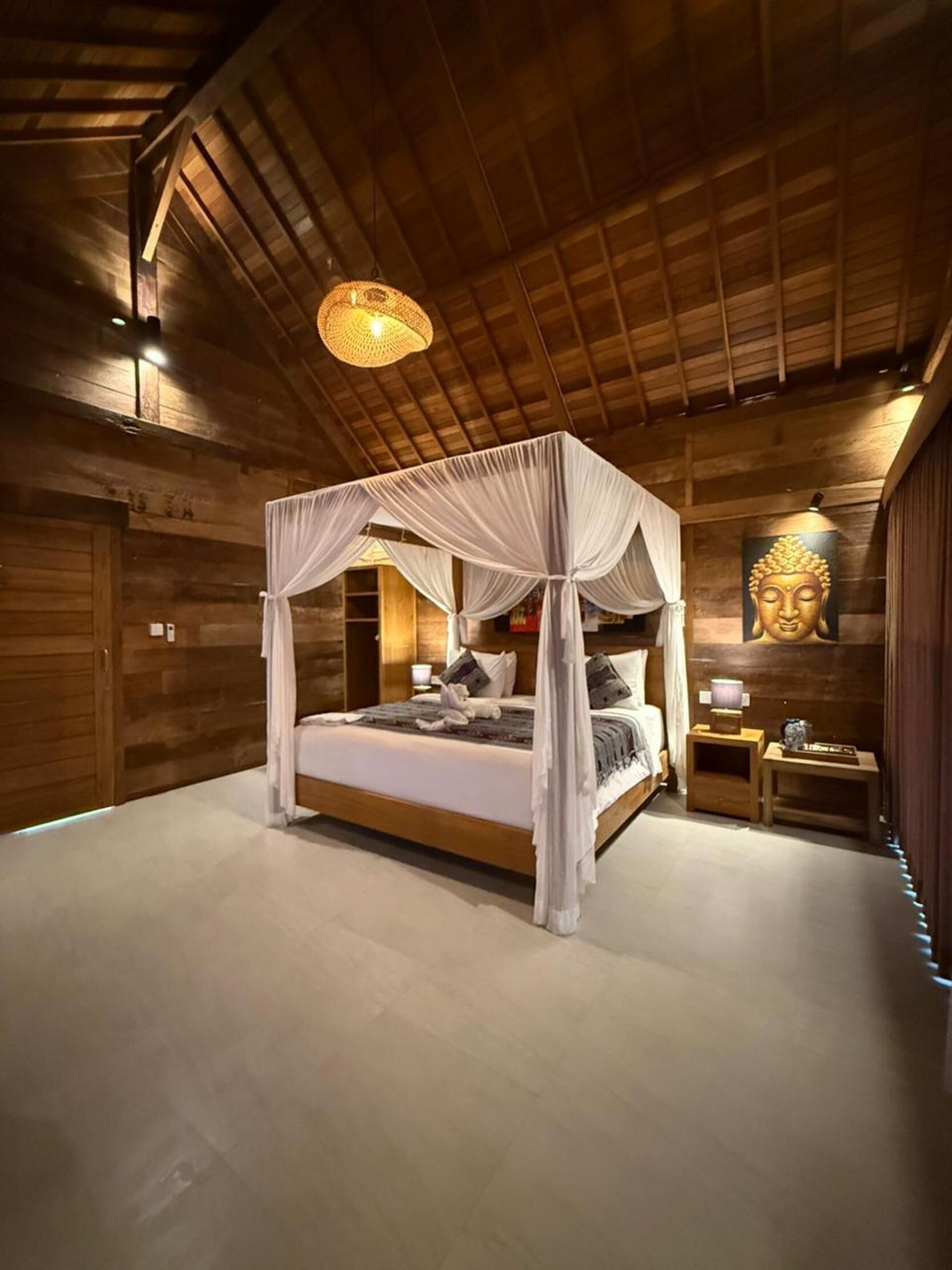 Ein hölzernes Zimmer mit einem Himmelbett und einer Buddha-Statue an der Wand.