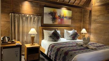 A wooden room with a bed, two bedside lamps, a small table with a kettle, and a painting on the wall.