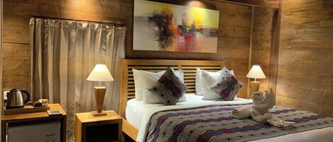Una habitación de madera con una cama, dos lámparas de noche, una mesita con un hervidor y un cuadro en la pared.