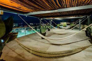 Eine Dachterrasse mit einer Hängematte, Topfpflanzen und Blick auf die Stadt bei Nacht.