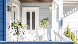 Een wit huis met een veranda, een deur met een decoratief glasraam en een kleine boom op de veranda.