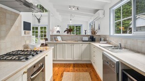 Een moderne keuken met witte kastjes, een gasfornuis, een vaatwasser en een groot raam met uitzicht op groen.