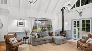 A cozy living room with a sectional sofa, a fireplace, and a large window overlooking a garden.