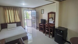 Habitación de hotel con cama, escritorio con ordenador, un refrigerador pequeño y puerta que da a un balcón.
