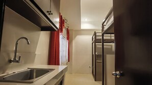 Una cocina compacta con un lavamanos de acero inoxidable, armarios blancos y una puerta de madera.