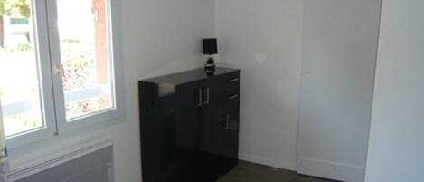 Una habitación con una cama, una ventana, un radiador, un armario negro y una puerta.