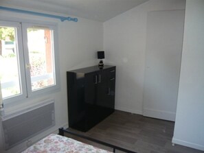 A room with a bed, a window, a radiator, a black cabinet, and a door. - Charming 6-Person Duplex with Garden, Terrace, and Pool Access in Le Grau-du-Roi (Le Grau-du-Roi)