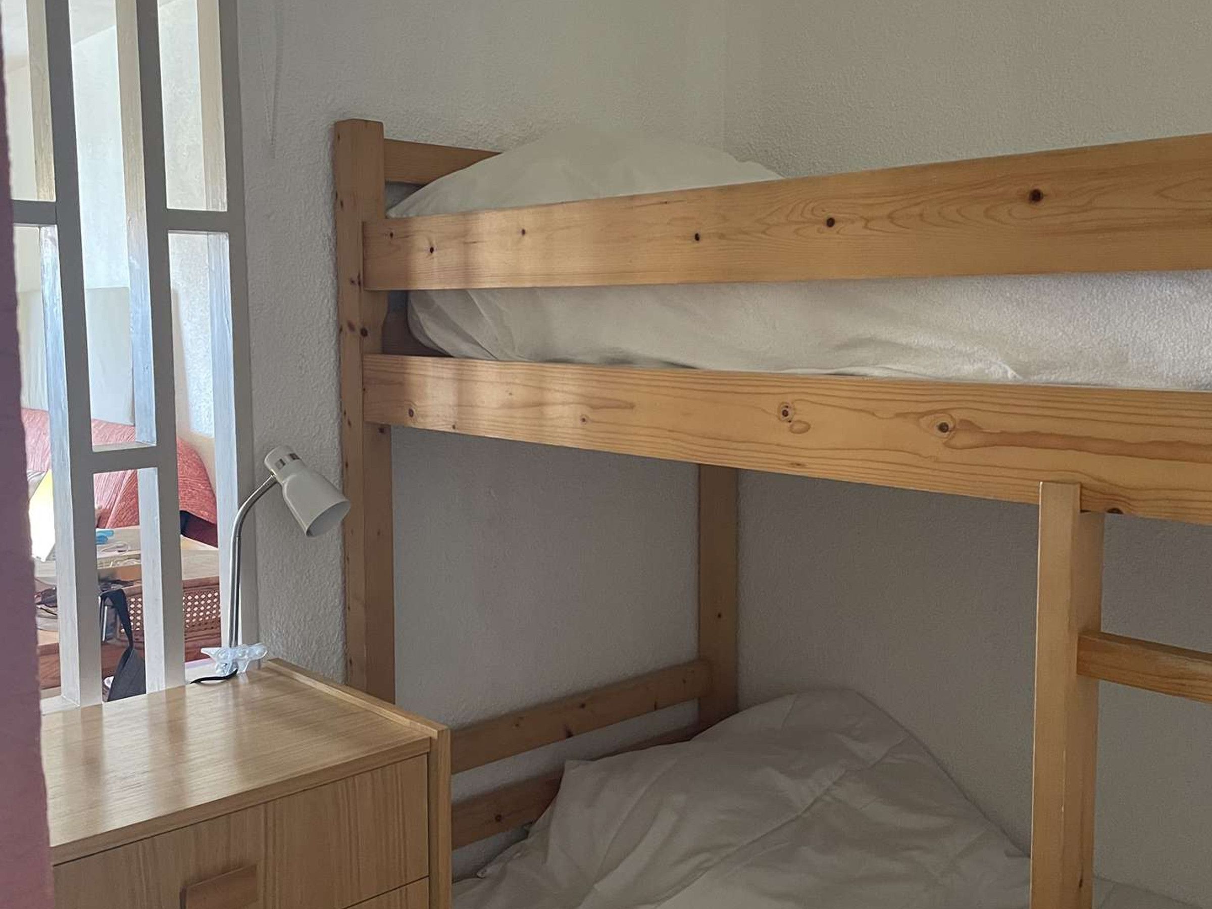 Un lit superposé avec une structure en bois, une table de chevet avec des tiroirs et une lampe.