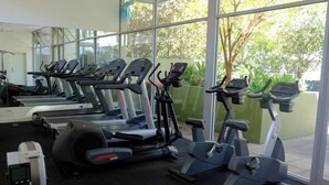 Un gimnasio con varias cintas de correr y bicicletas estáticas, ventanas amplias con vistas a espacios verdes.