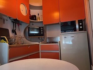 A compact kitchen with a built-in microwave, a small refrigerator, and a sink. - Cozy 1BR Apartment with Terrace, Parking, Next to Beach and Shops (Port Camargue)