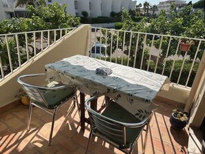 A balcony with a table and two chairs, a potted plant, and a view of buildings and greenery. - Cozy 1BR Apartment with Terrace, Parking, Next to Beach and Shops (Port Camargue)