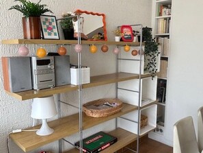 Een kamer met een houten bureau, een witte lamp en planken met diverse spullen, waaronder een mand en een boek.