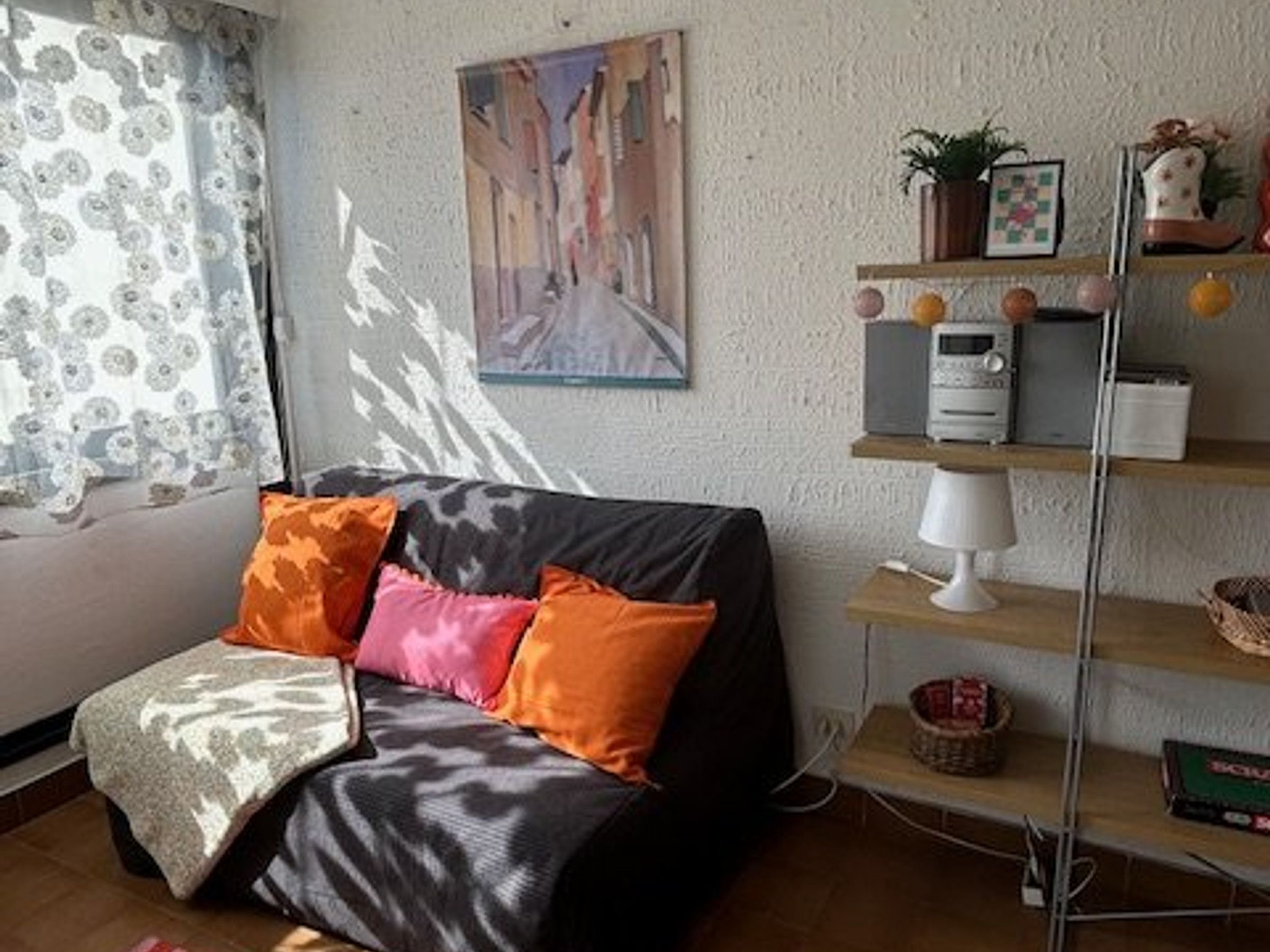 Een woonkamer met een bank, een lamp, een plank met decoratieve objecten en een schilderij aan de muur.