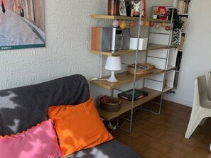A living room with a sofa, a small table, and a shelf with various items. - Cozy 1BR Apartment with Terrace, Parking, Next to Beach and Shops (Port Camargue)