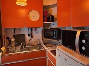 Een kleine keuken met een spoelbak, een magnetron en een fornuis.