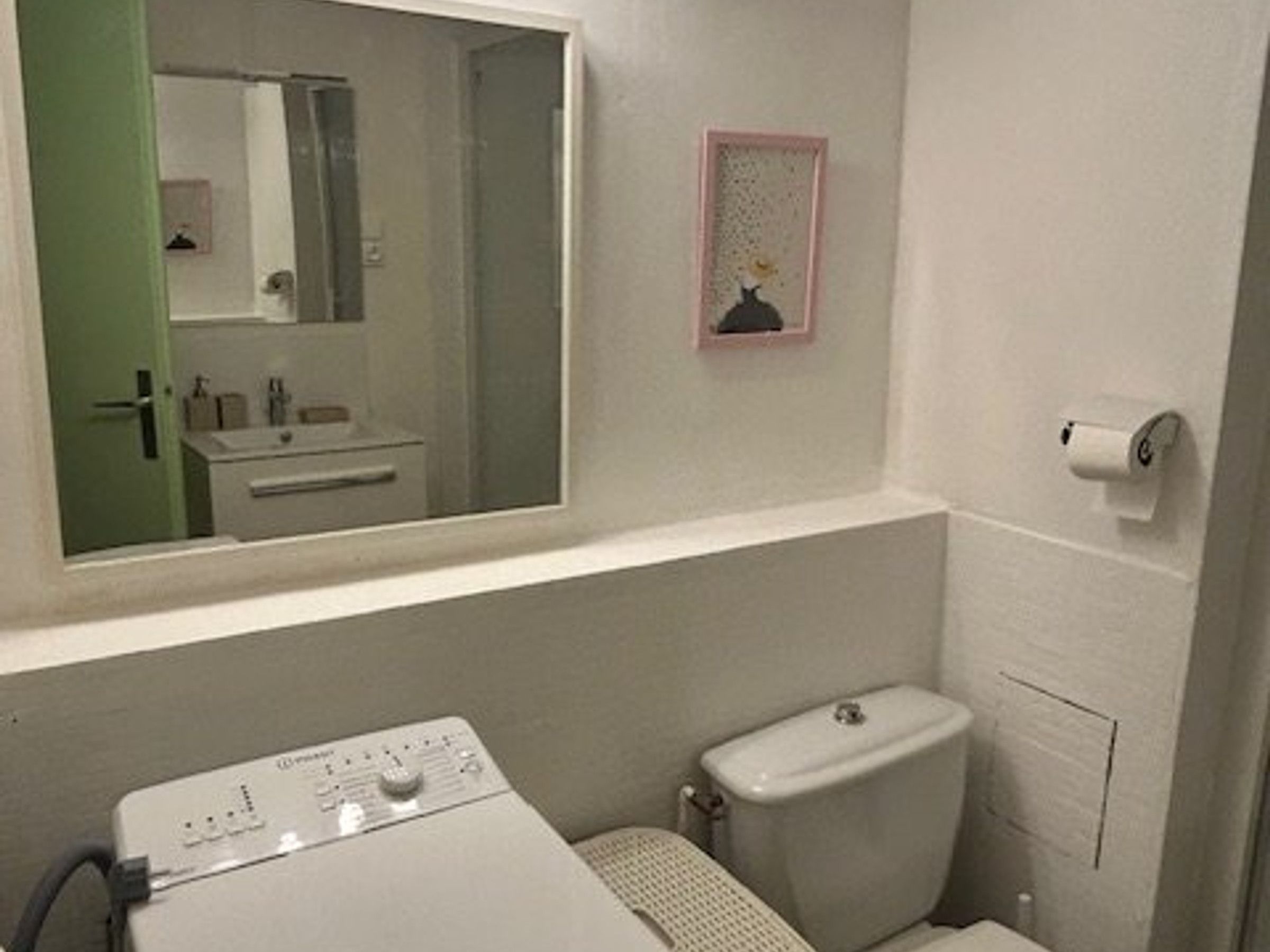 A small bathroom with a toilet, a sink, a mirror, and a washing machine.