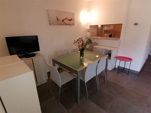 A compact living space with a dining table, chairs, a flat-screen TV, a small kitchen area, and a red stool. - 2-room apartment with private parking, 600m from shops (Port Camargue)