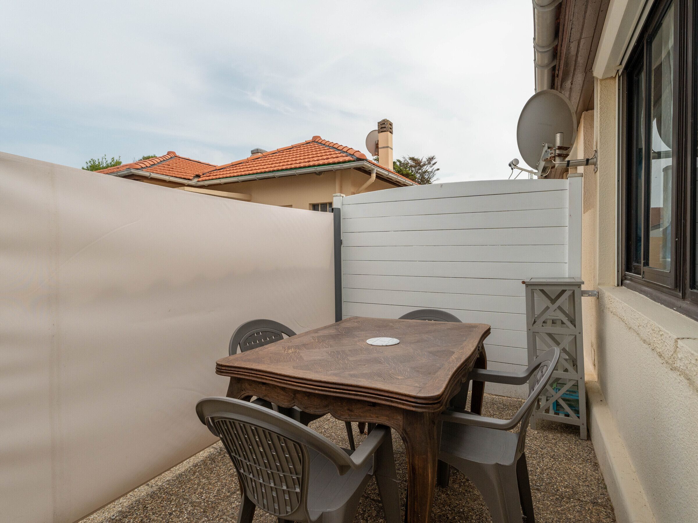 A patio with a wooden table and chairs, a white partition, and a satellite dish.