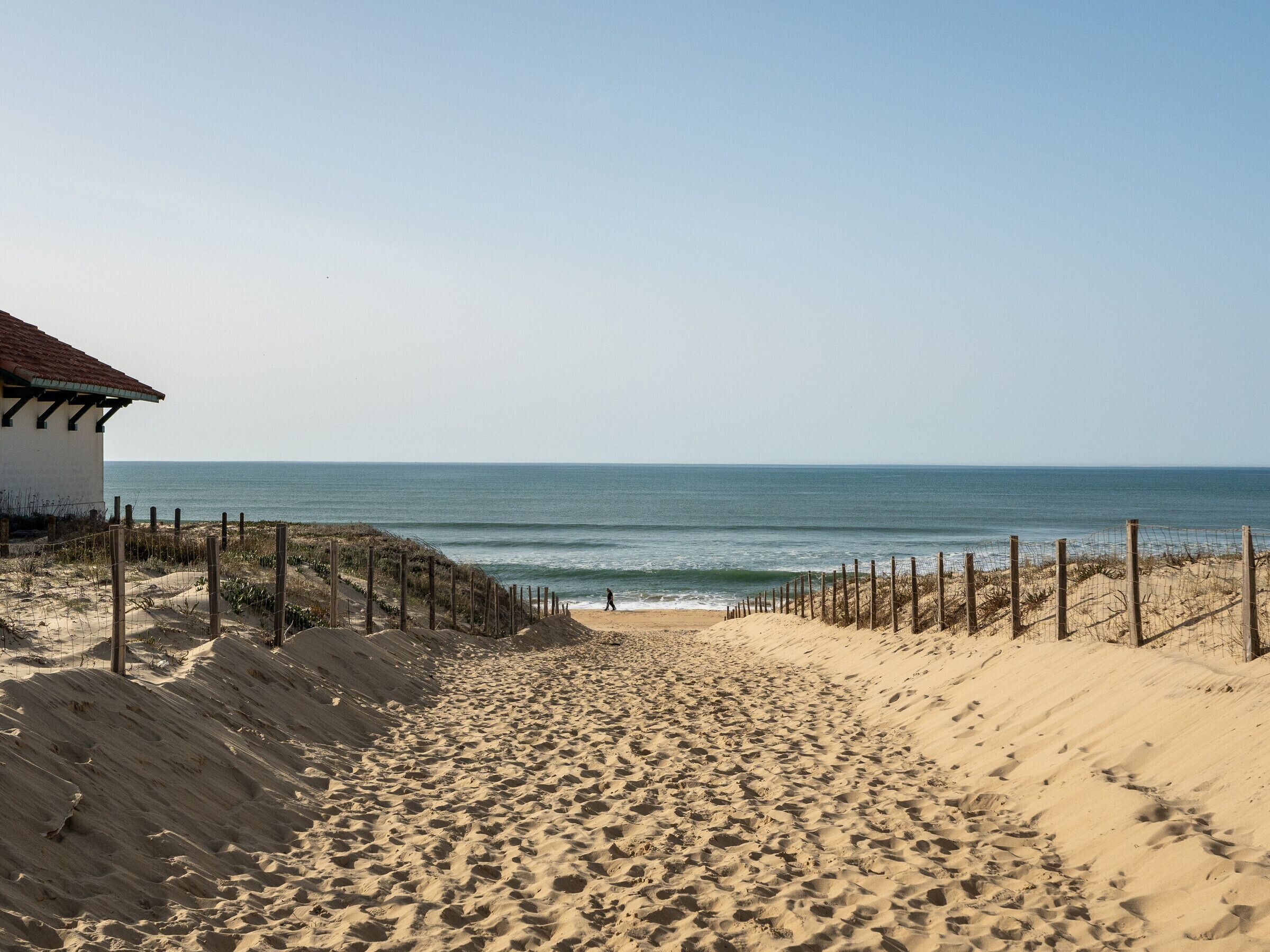 A sandy beach with a wooden fence and a building with a red roof.