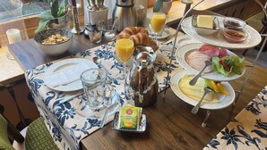 Desayuno con cruasanes, jugo de naranja y una variedad de quesos y embutidos sobre una mesa con mantel floreado.