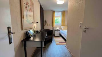 A hotel room with a desk, a bed, a nightstand, a lamp, a picture frame, and a window with curtains.