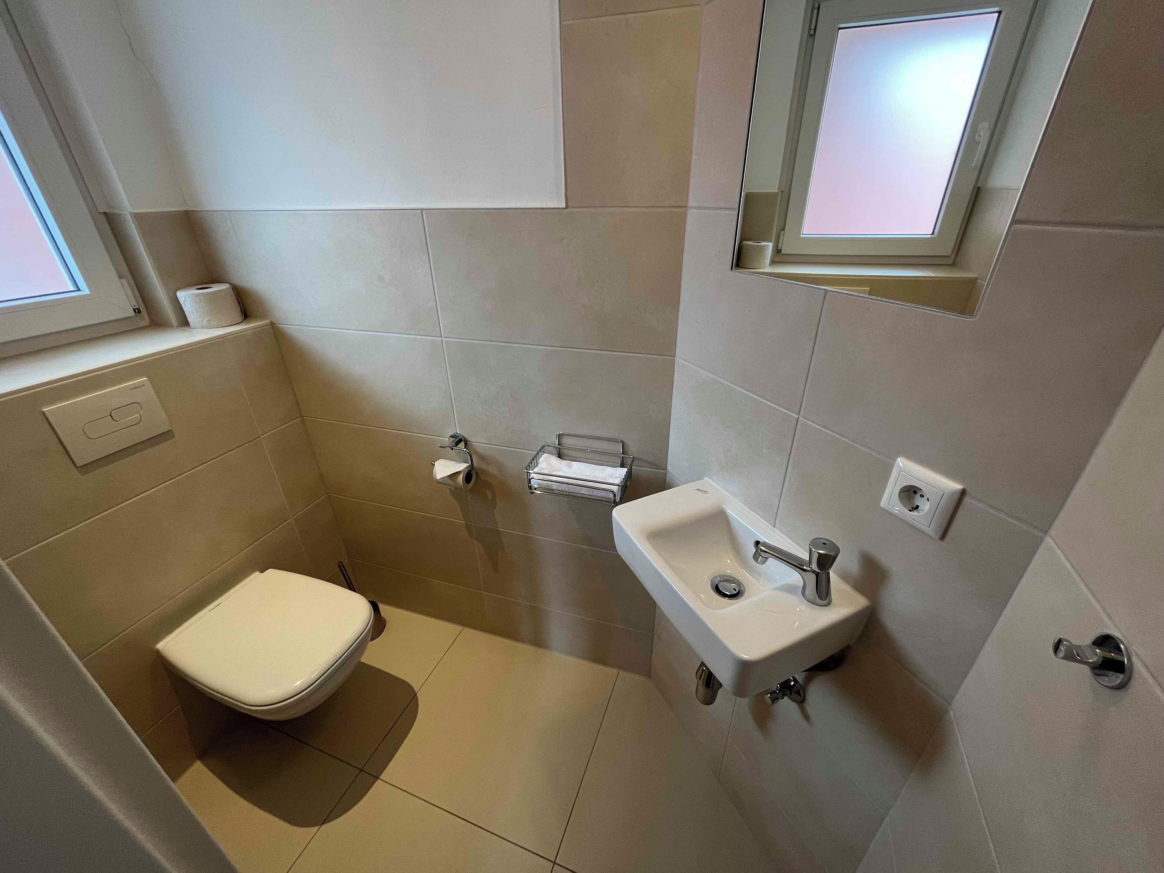 Une petite salle de bain moderne, équipée de toilettes, d’un lavabo et d’une fenêtre située au-dessus du lavabo.