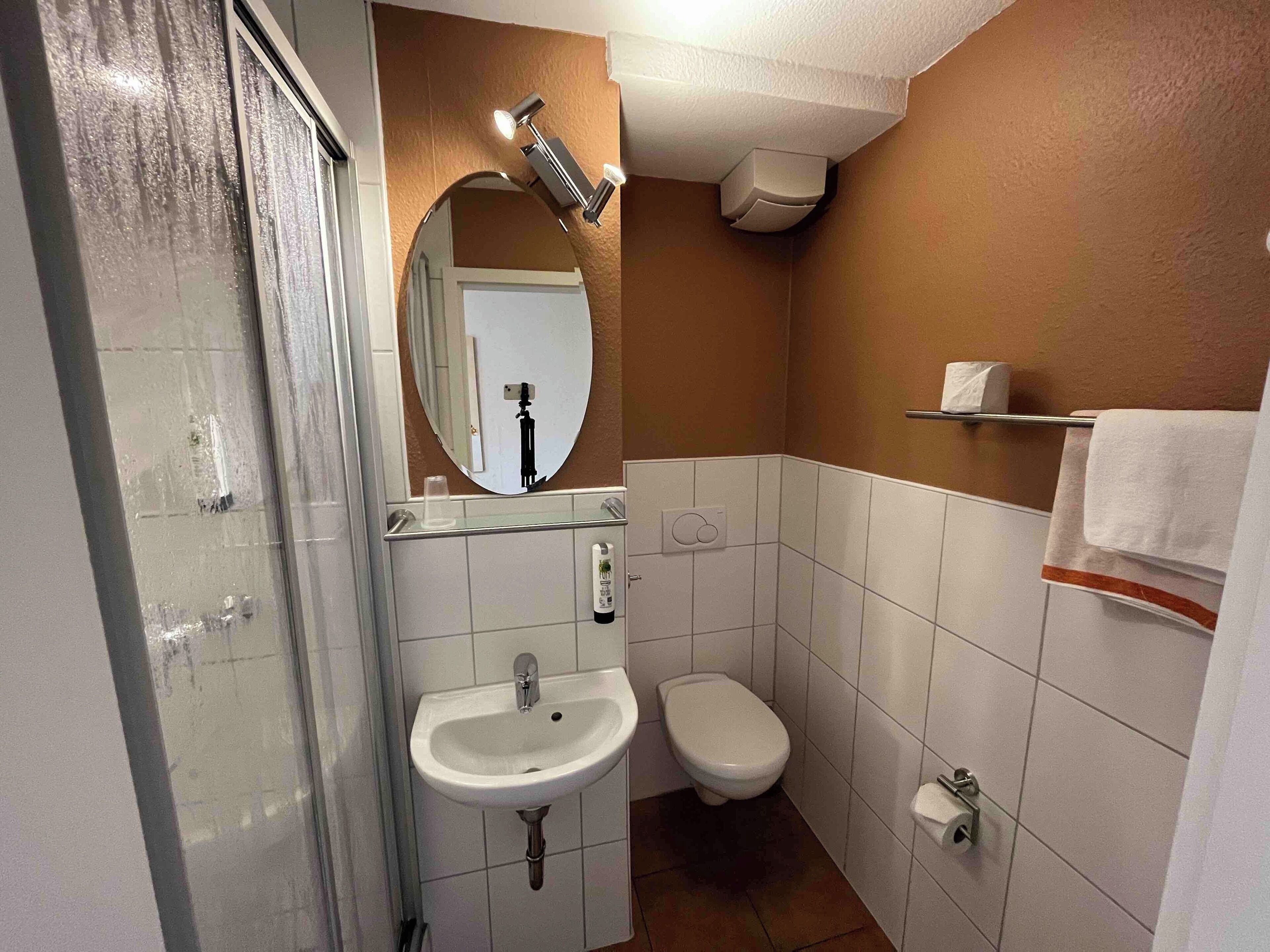 Ein Badezimmer mit Duschkabine aus Glas, Waschbecken in Weiß, Toilette und einem Spiegel mit integrierter Beleuchtung.