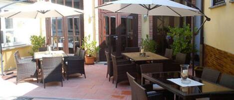 Un espace extérieur aménagé en terrasse, avec des tables et des chaises, des plantes en pot et des parasols pour créer de l’ombre.