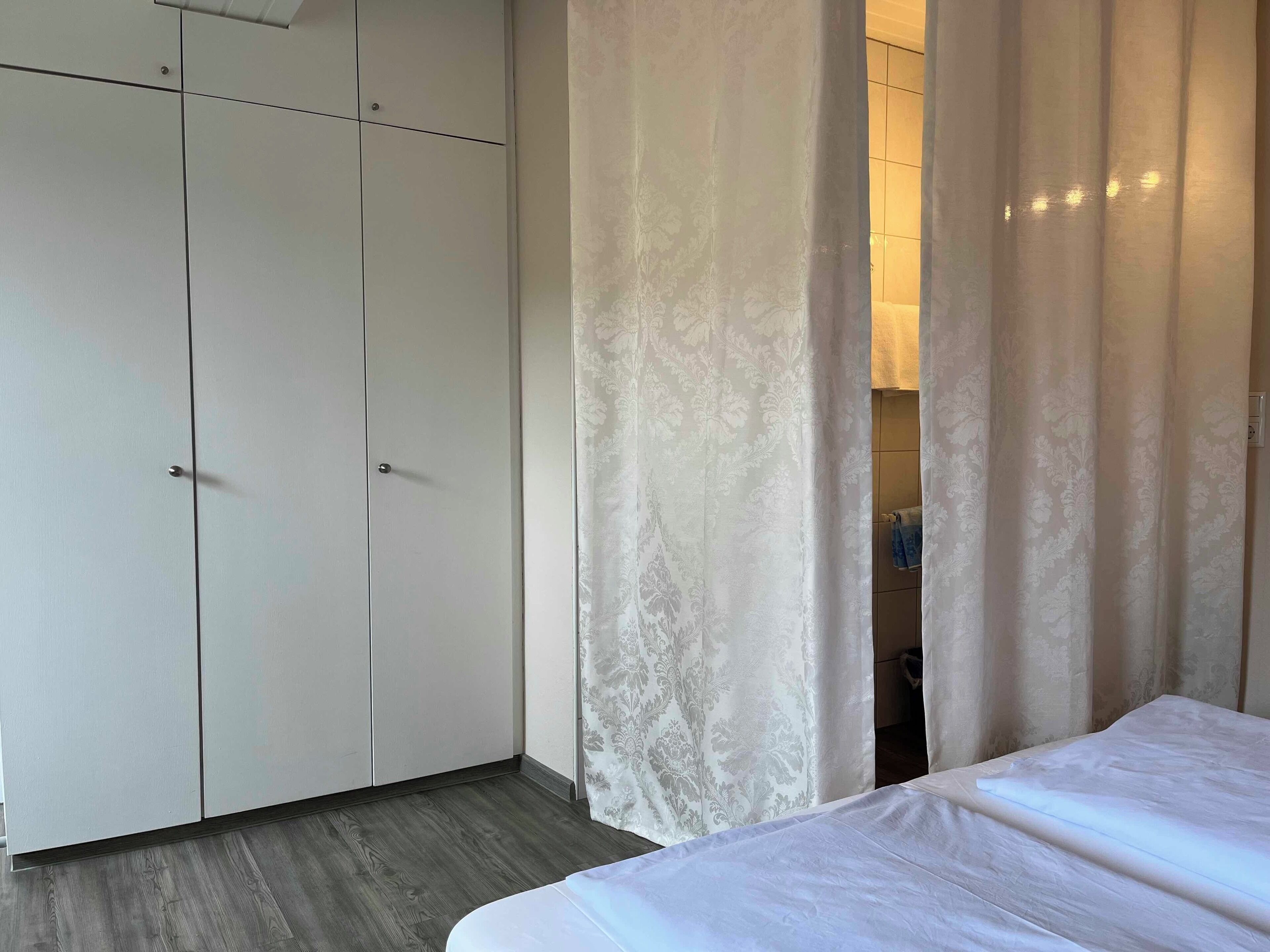 Un dormitorio con una cama, un armario y un baño visible tras una cortina.