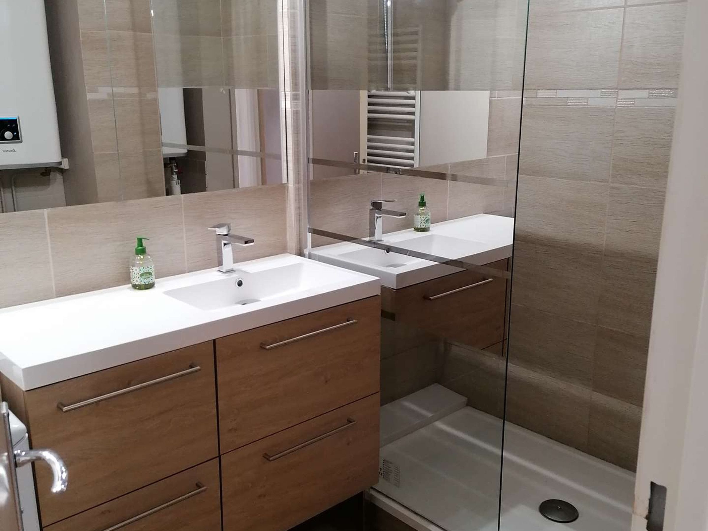 A modern bathroom with two sinks, a glass shower enclosure, and a mirror.