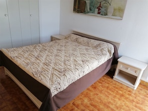 A bedroom with a bed, a nightstand, a dresser, and a wall-mounted shelf with decorative items.
