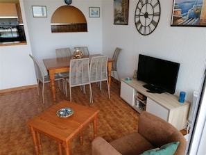 A living room with a television, a dining table with chairs, and a sofa.