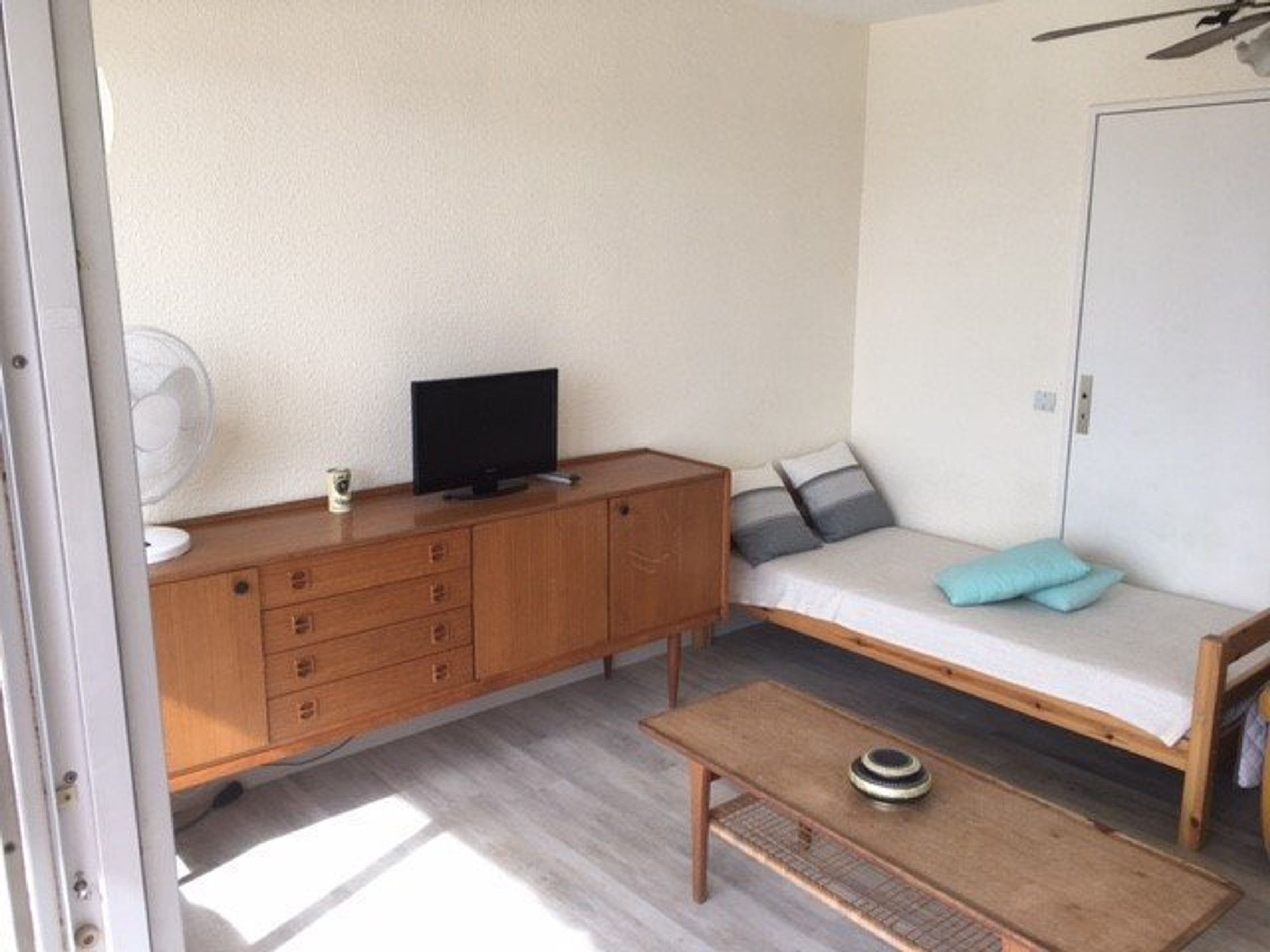 Ein kleiner, kompakter Raum mit einem Holzschrank, einem Fernseher, einer Couch mit Kissen und einem kleinen Tisch.
