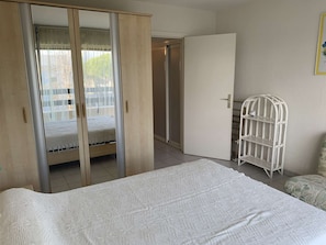 Ein Schlafzimmer mit einem Bett, einem Kleiderschrank, einer Tür zu einem anderen Raum und einem weißen Regal.