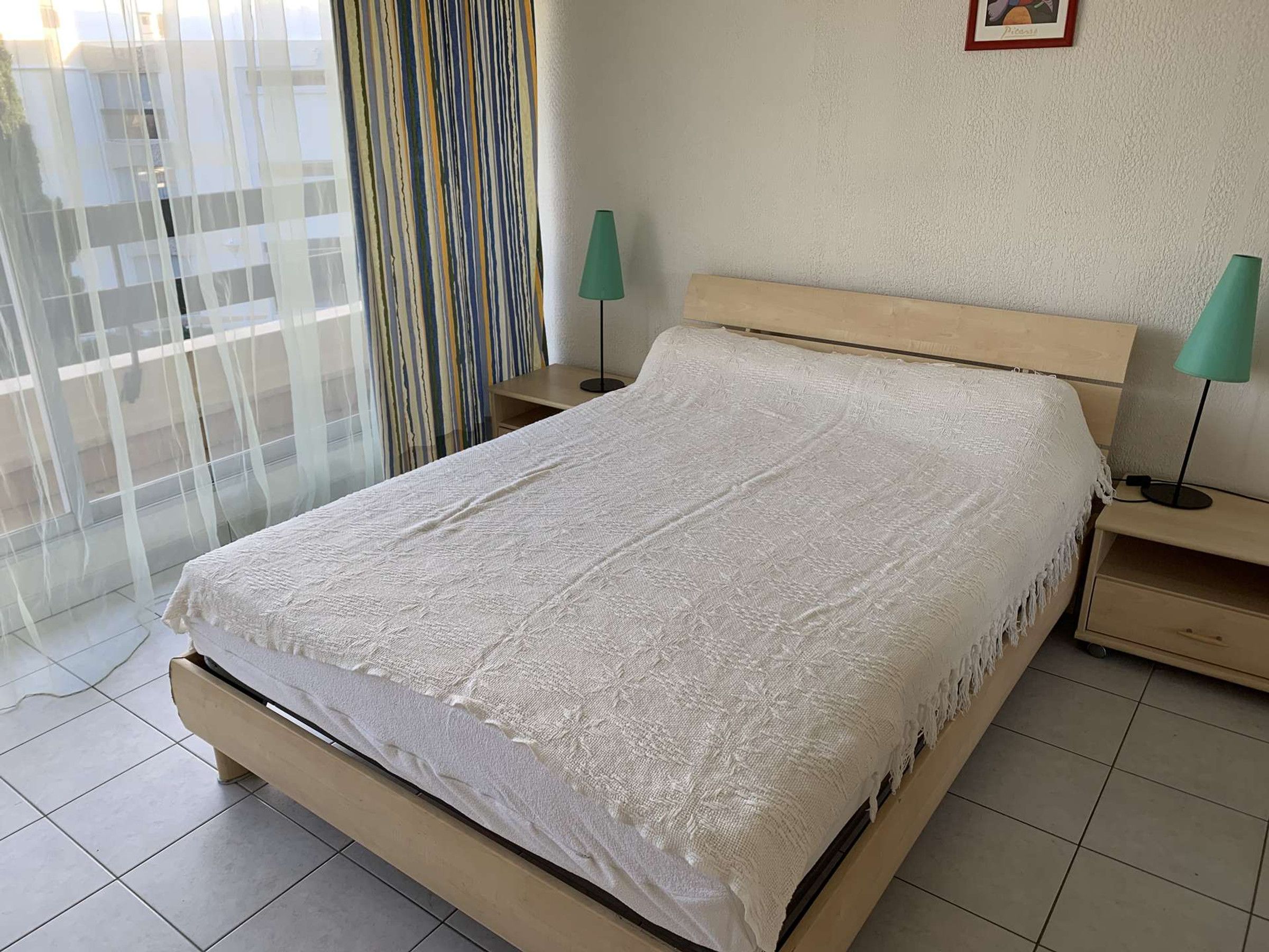 A bed with a white textured bedspread, a wooden headboard, and two bedside tables with lamps.