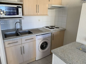 A compact kitchen with a washing machine, a microwave, and a stove.