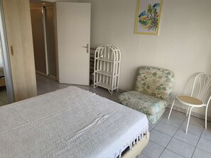 A bedroom with a bed, a chair, a wardrobe, and a shelf. - Charming 2-Room Apartment with Pool, Terrace, and Parking Near Port Camargue (Port Camargue)