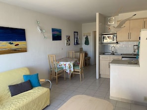 A compact living space with a kitchenette, a dining area with a table and chairs, and a bed with a quilted cover.