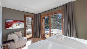 Una habitación de hotel moderna con una cama grande, un área de descanso y vistas a un paisaje nevado a través de puertas de cristal.