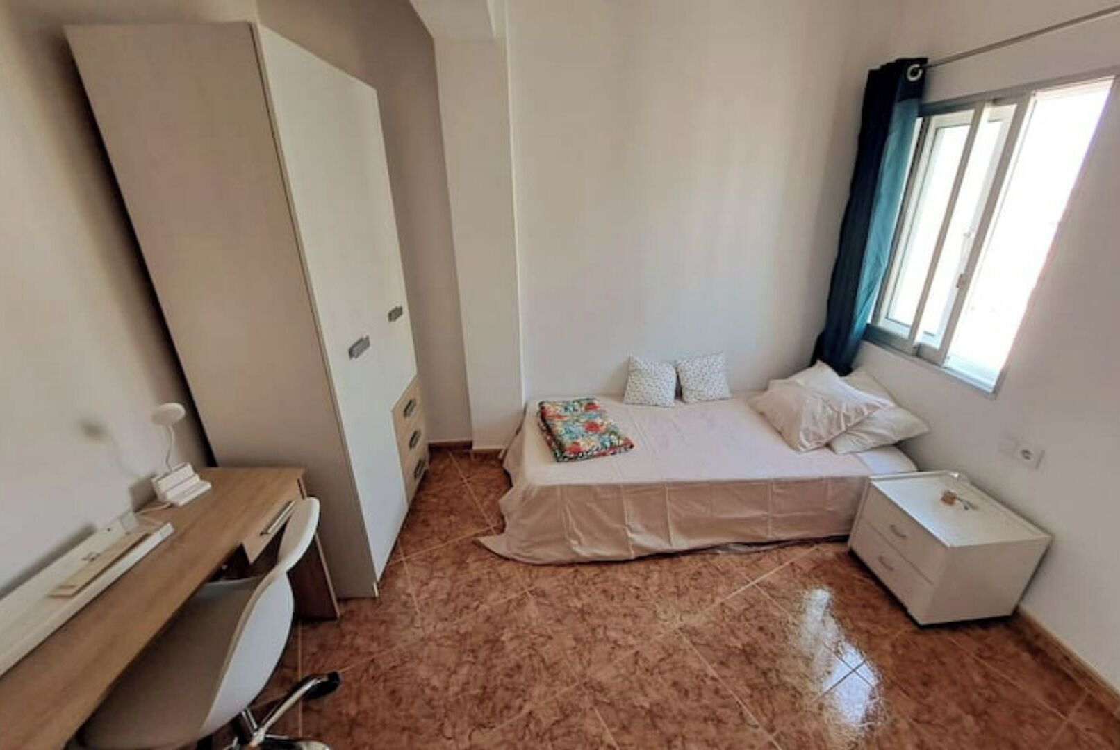 A small, clean room with a bed, a desk, and a window.