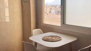 Une petite pièce avec une table et deux chaises, une fenêtre donnant sur des immeubles et un panneau accroché au mur.