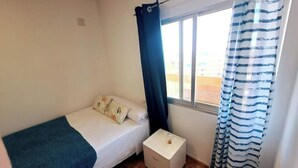Une petite chambre avec un lit simple, une fenêtre, une table de chevet et un rideau.