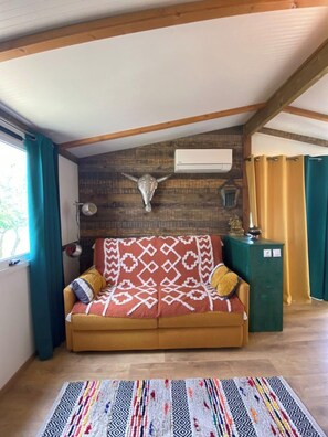 A cozy room with a wooden ceiling, a brown sofa with patterned cushions, a decorative wall-mounted bull's head, and a green cabinet.