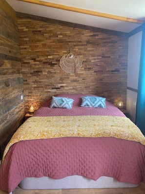 A bedroom with a wooden wall, a bed with a pink and gold bedspread, and two decorative pillows.