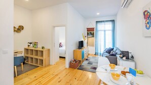 A modern living room with a wooden floor, a dining area with a table set for two, a sofa, and a TV. - Balcony City Views (Porto)