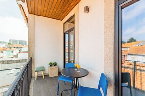 Un balcon avec une table ronde, des chaises bleues et un petit tabouret.