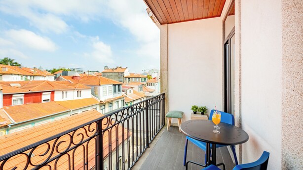 A balcony with a table and chairs, a potted plant, and a view of the cityscape. - Balcony City Views (Porto)