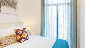 A bedroom with a large bed, a headboard, a bedside table, and a window with curtains. - Balcony City Views (Porto)